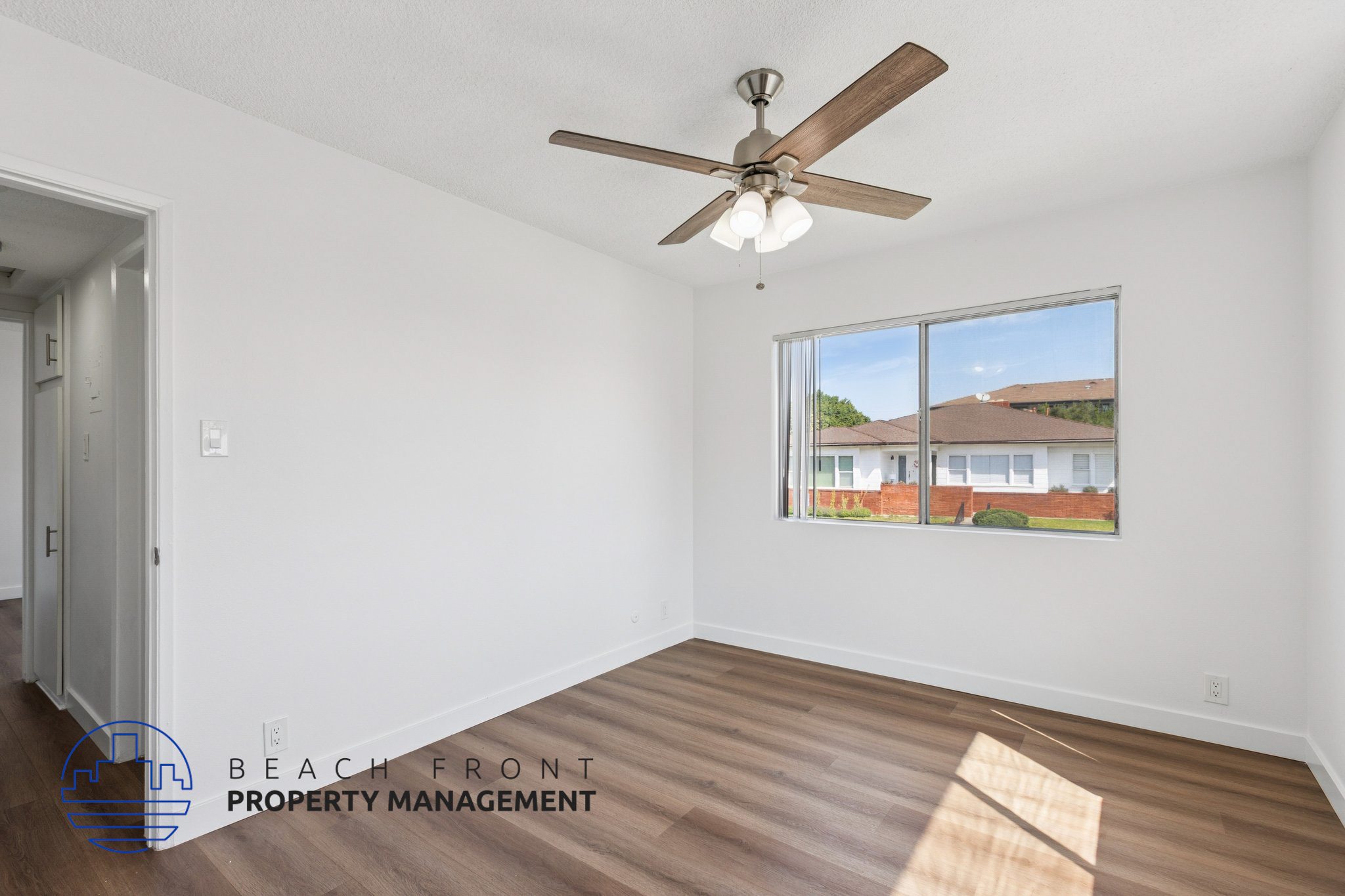 A room with a ceiling fan and a window showing a view of a building.